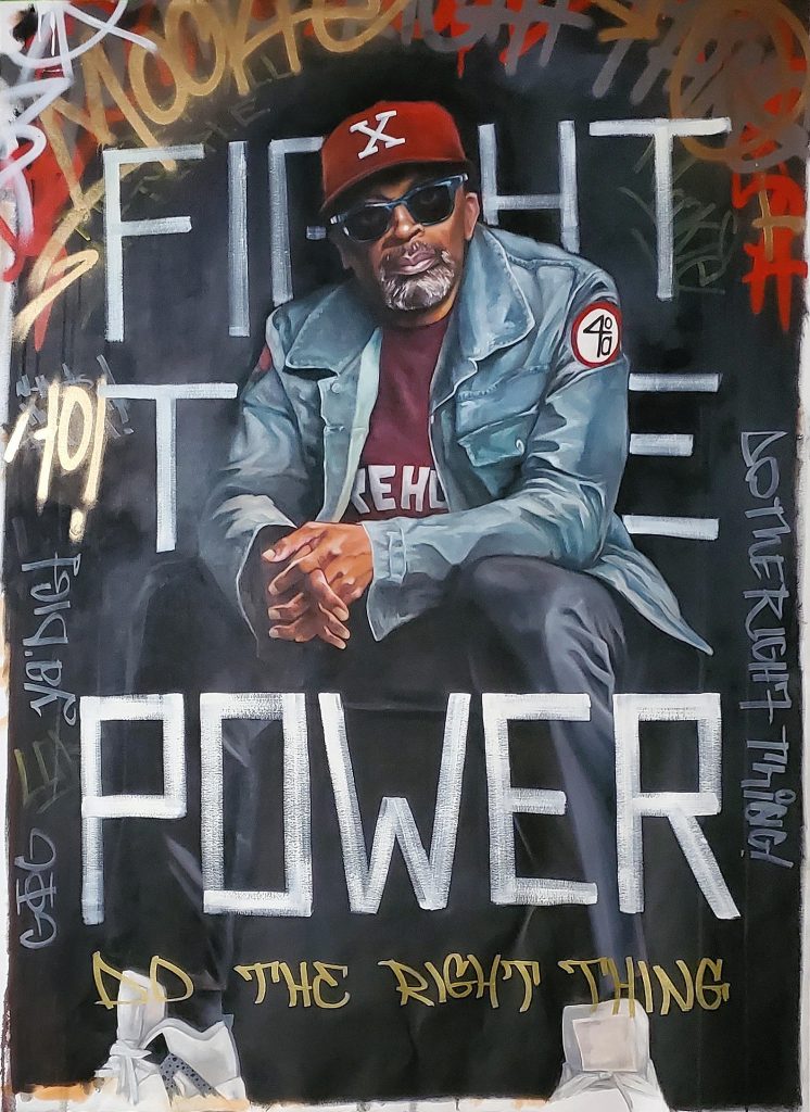Legendary filmmaker and culture crafter, Spike Lee sits in a “X” and Morehouse college t-shirt in front of the words of the iconic song “Fight the Power”. Spike Lee has always pushed the limits of storytelling and telling the truth of what goes on under the American sun in its relation to Blackness and race in general. The graffiti is used to express the urban grit it takes to push the limits of any art form