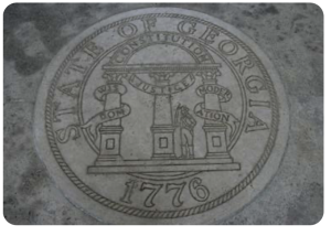 A picture of the Seal of the State of Georgia (dated 1776), engraved into stone. The seal has three columns labeled ‘wisdom,’ ‘justice,’ and ‘moderation,’ with an arch labeled ‘Constitution’ connecting the three