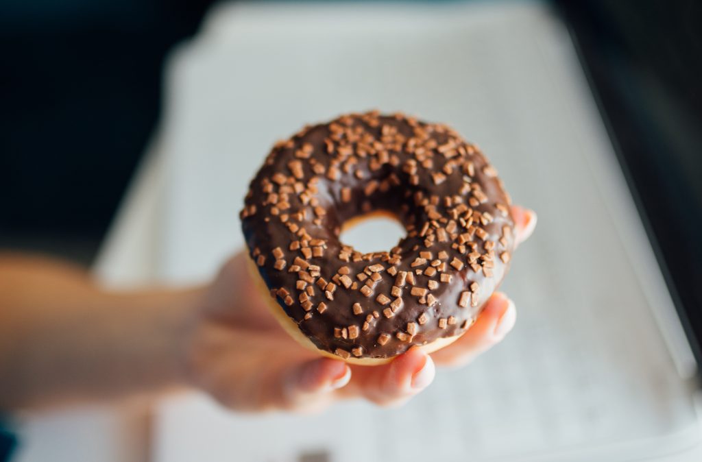 A photograph of a person's hand holding up a donut with chocolate frosting.