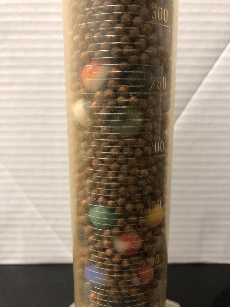 A photograph zoomed in of a the mixture of BBs and marbles in a graduated cylinder. The small BBs clearly take up space in between the large marbles.