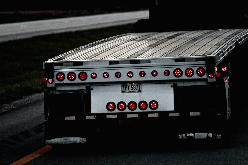 A photograph of the back of an empty flatbed truck. The flatbed has a visible upward curve to it.