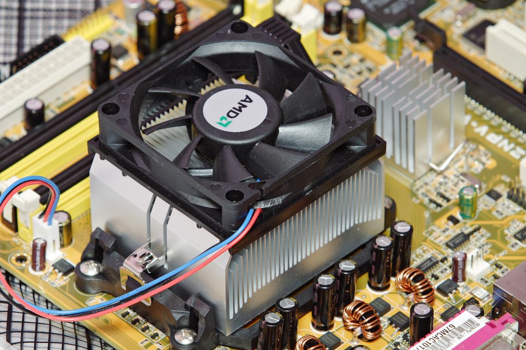 A photograph of a heatsink, a large metal object with many ribs to increase surface area. A fan is placed over top. The heatsink is placed on a computer processor that is attached to a computer motherboard, containing many electronic components.