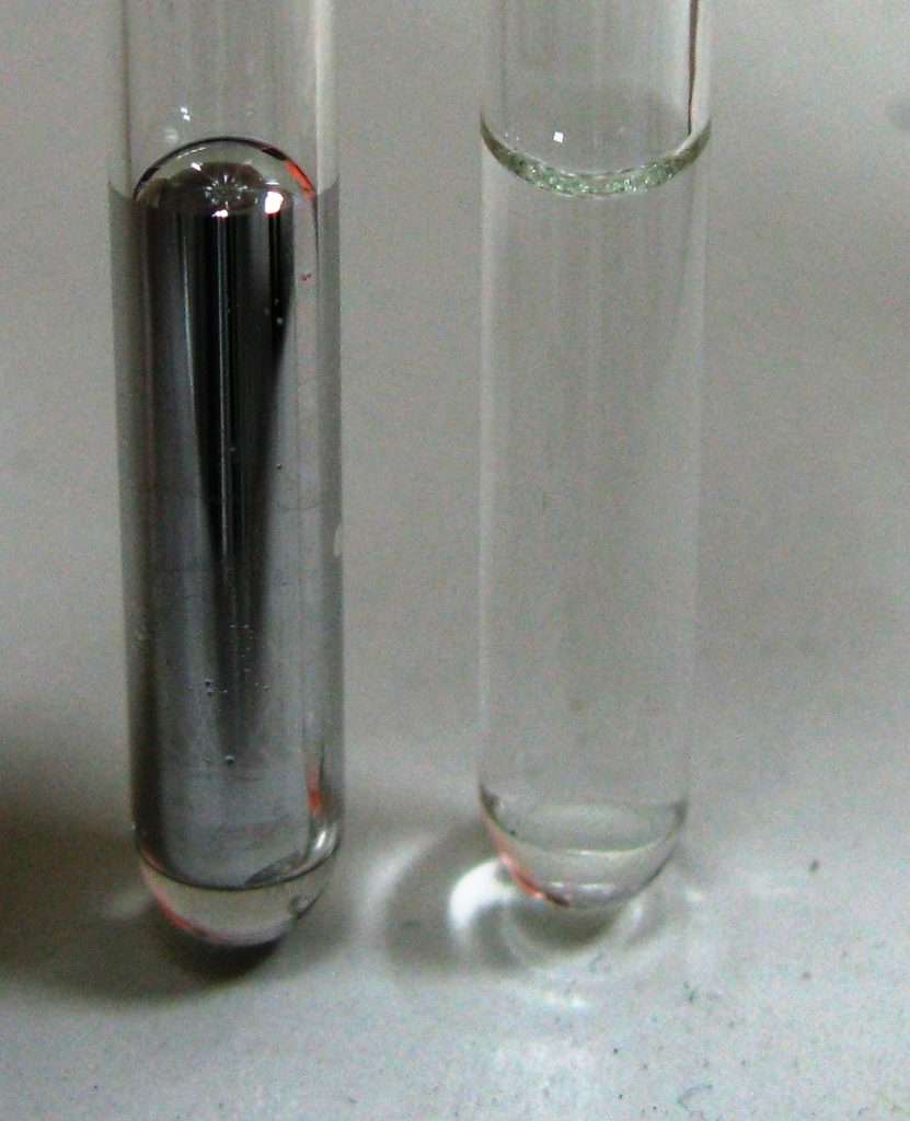 A photograph of two glass tubes. On the left the tube is partially filled with mercury, which creates a convex meniscus. On the right, the tube is partially filled with water, which creats a concave meniscus.