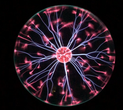 A photograph of a plasma ball. There are purple arcs of electrical discharge (plasma) shooting from the center of the ball to the glass sides. The surrouding areas are black to focus on the electrical discharge.