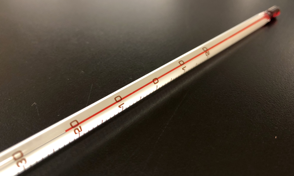 A photograph of an analog thermometer. Red dyed alcohol in a long, narrow glass tube has is at the level of about 22 degrees Celsius, indicated by markings on the side of the glass tube.