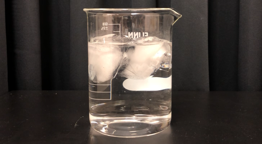 A photograph of ice cubes floating in a beaker filled with water.