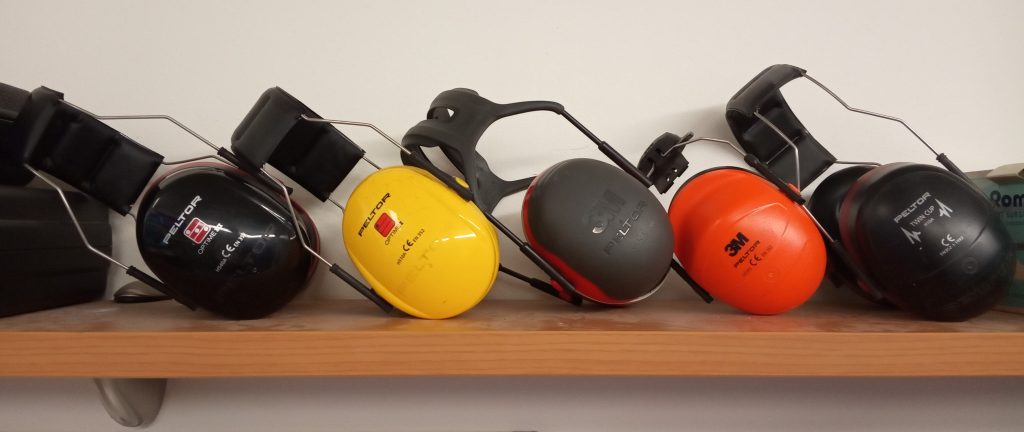 A photograph of five sets of earmuffs sitting on a bench. Each one is a different color.