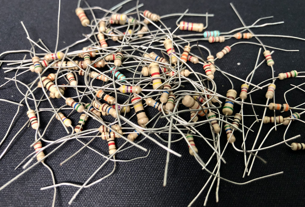 A photograph of several dozen resistors, which are small cylinders with colored stripes on them, with axial metal leads protruding from either end of the cylinder.