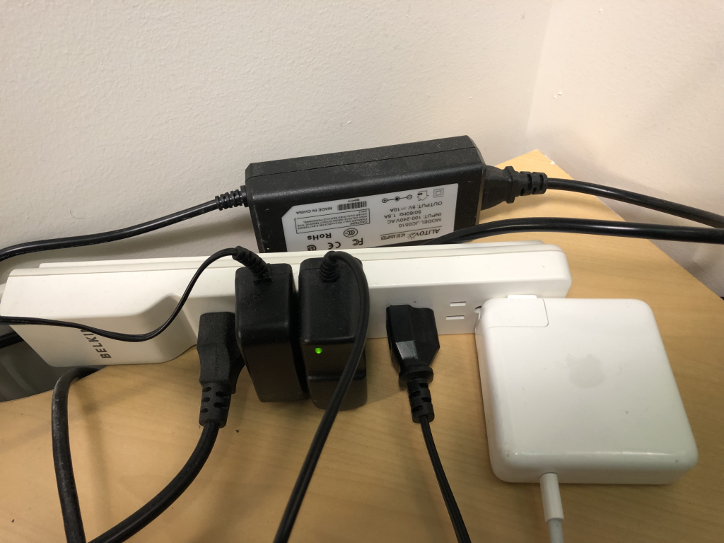 A photograph of a power strip with multiple charging cables connected. Three of the charging cables have a large chunky block of plastic on the plug end, known colloquially as a "wall wart." An additional charging cable has the "wall wart" positioned halfway up the cable.
