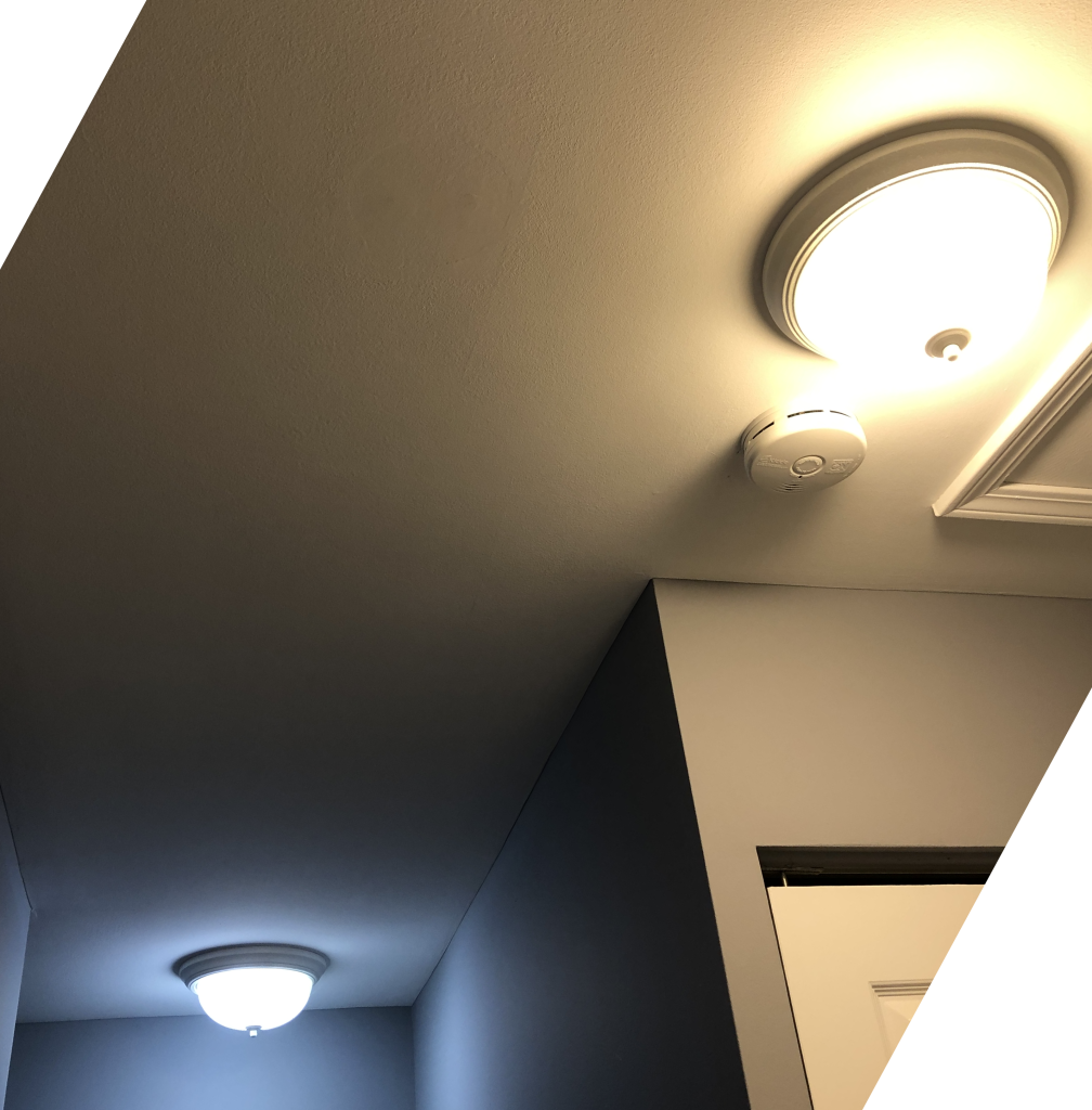 A photograph of two light fixtures affixed to a ceiling in a house. One of the light fixtures contains a "cool" bulb glowing bluish-white, and the other fixture contains a "warm" bulb glowing yellowish-white.