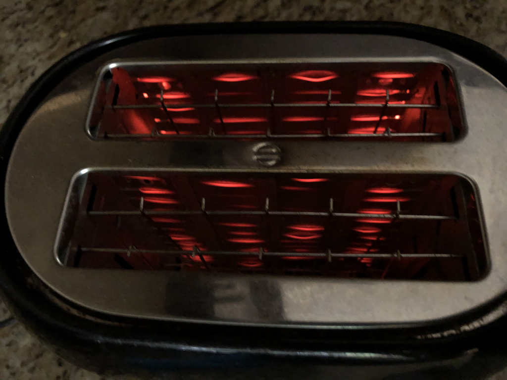 A photograph of a toaster seen from the top. The heating elements are glowing red/orange.