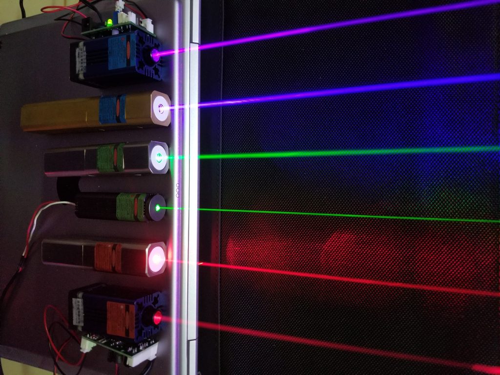 A photograph of six lasers all emitting light at different colors. The individual laser colors are red, red, green, green, blue, and violet.
