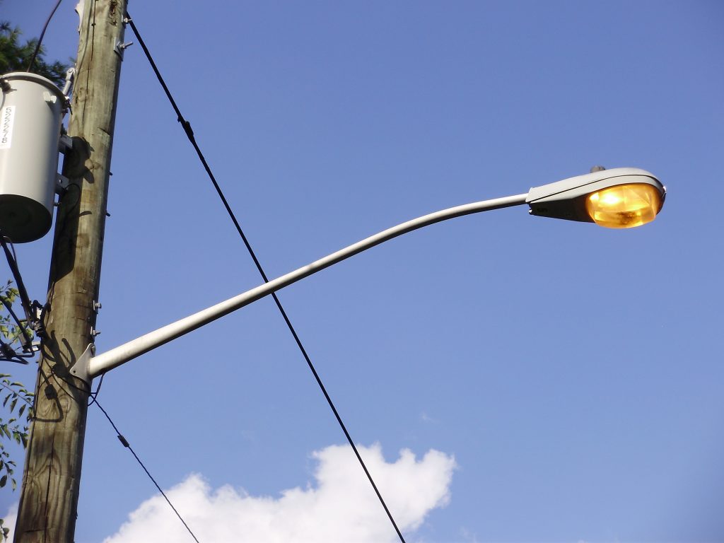 A photograph of a sodium vapor street lamp which is on and emitting a yellow colored light.
