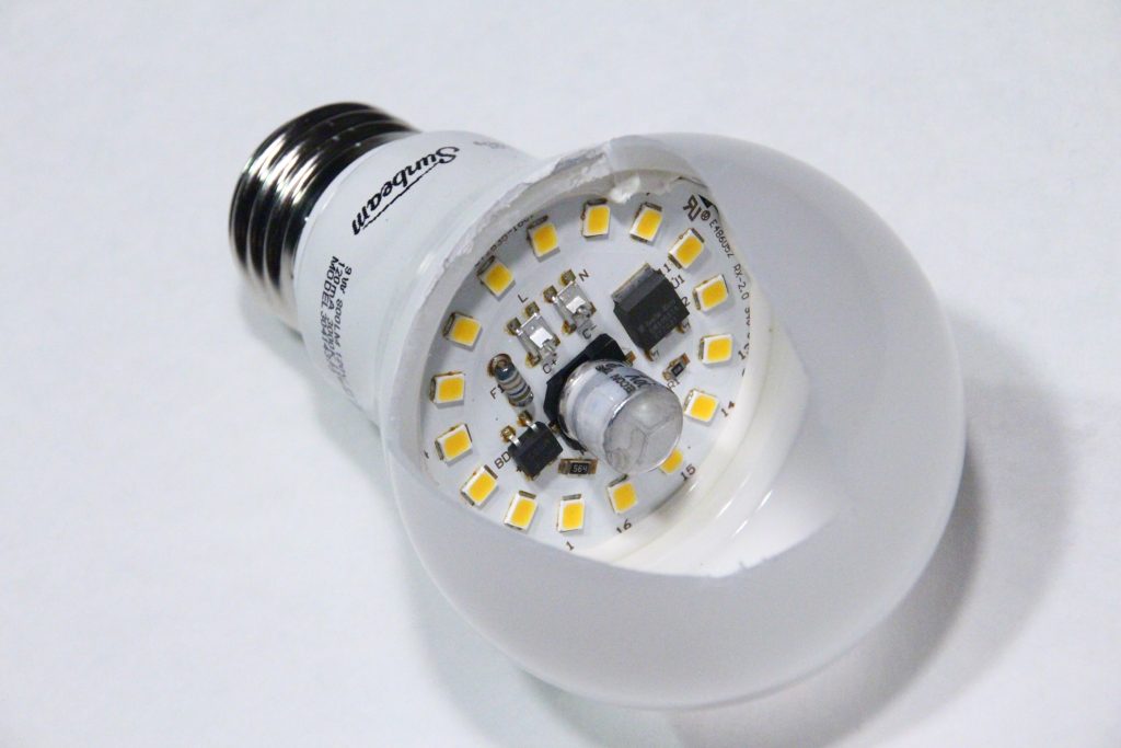 An LED light bulb is photographed with the glass bulb broken on purpose to show the circuitry in the container. There are 16 individual LEDs as well as several electronics components.