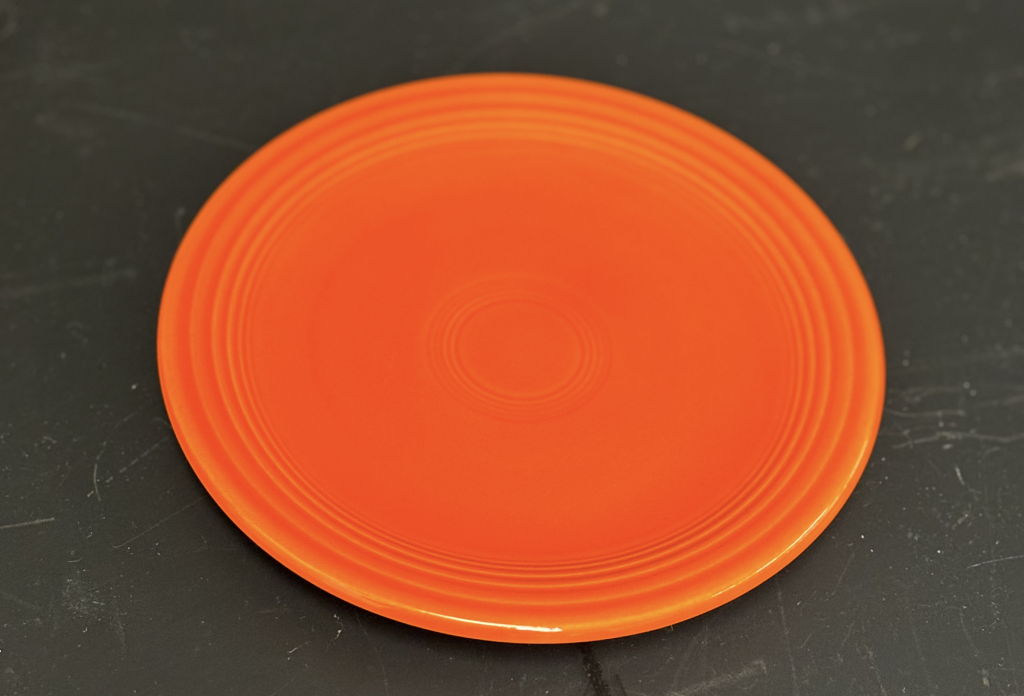 A photograph of a reddish-orange circular dinner plate. The background is black.