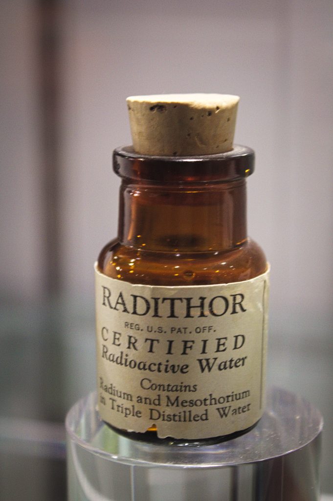 A photograph of an empty small amber bottle labeled "RADITHOR, CERTIFIED Radioactive Water, Contains Radium and Mesothorium in Triple Distilled Water."