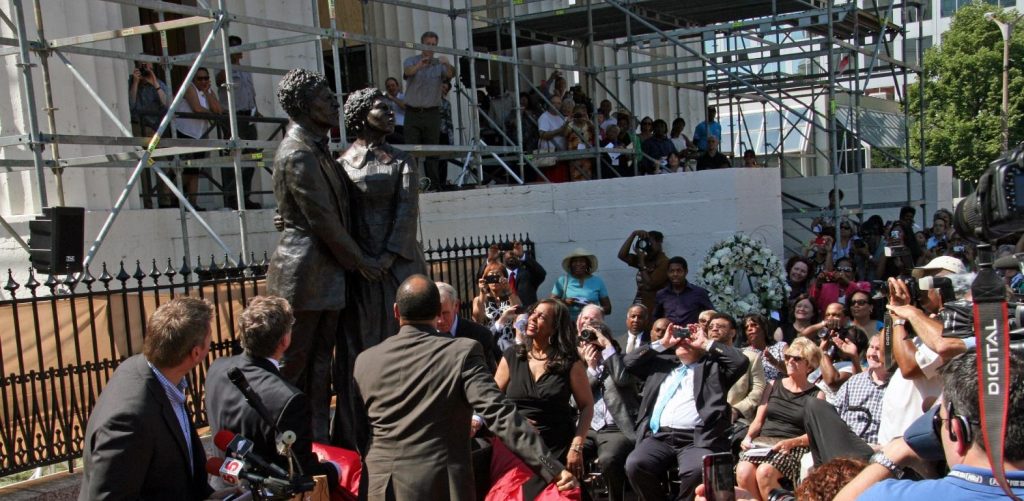 A group of people, including reporters, gathered around a new statue of Dred and Harriet Scott
