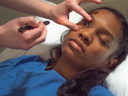 Assessing an unconscious client's pupillary light reflex.