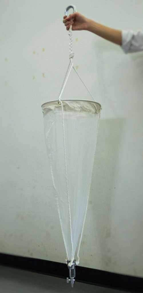 A hand holds a long white plankton net.