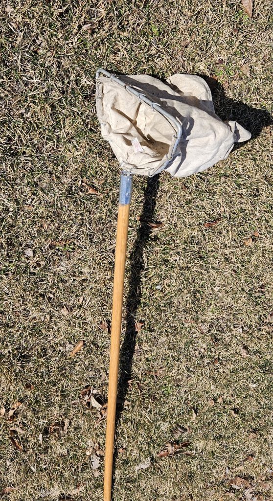 A D-frame dip net with a long wooden handle and a net suspended from a D-shaped metal ring.