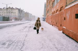 A warmly bundled woman walks her dog along a snowy street in Norilsk, Russia, at -32°C.