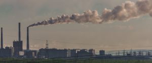 A gray photo shows a long plume of steam/smoke emanating from a high factory chimney in Norilsk, Russia.