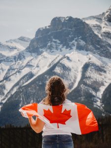 Photograph of Canadian woman and flag in front of snowy mountain in Alberta, Canada.