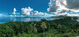 Photograph of Chuuk Lagoon in Micronesia, featuring blue sky with white clouds and blue water with adjacent green trees.