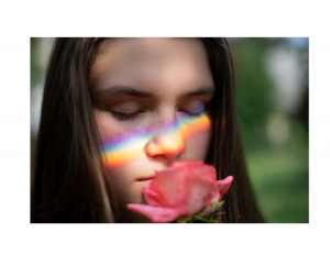 Girl smelling a rose with a rainbow across her face.
