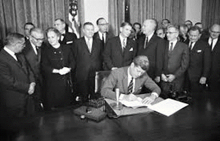 black and whote photography of JFK (sitting) signing a bill surrounded mainly by men