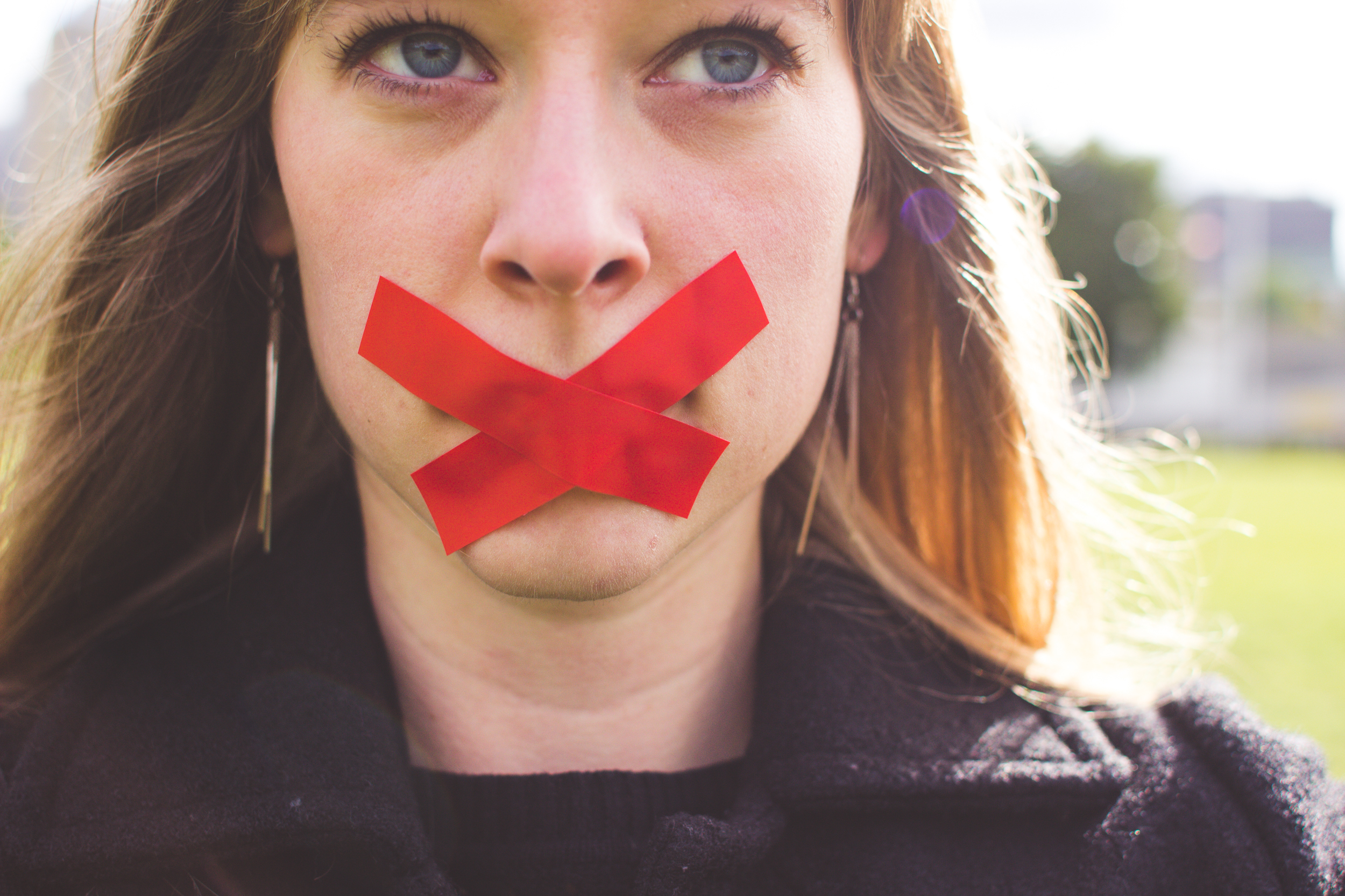 color photograph of a woman with a red X tape across her mouth